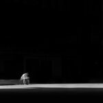 A lone man sitting on a bench, captured in striking black and white, conveying solitude and contemplation.
